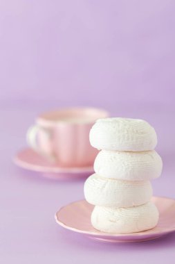 Zephyr'i dessrt pembe plaka, pastel mor zemin üzerine sütlü kahve fincan beyaz. Güzel tatlılar. Dikey afiş, tebrik kartı için doğum günü, düğün. Fotoğraf kadar kapatın. Seçici odak