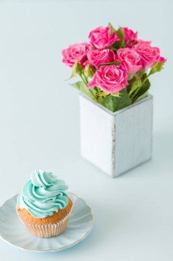 Kremalı cupcake ve retro eski püskü şık vazoda pembe gül buketi dikey afiş ile süslenmiş pastel mavi.