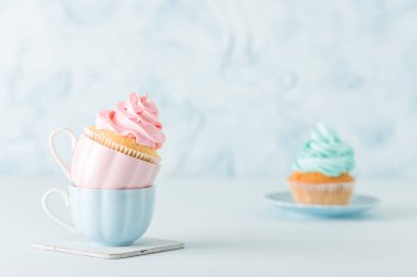 Yumuşak pembe ve mavi krem dekorasyon pastel mavi zemin üzerine iki bardak ile cupcakes.