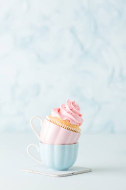 Pastel mavi zemin üzerine iki bardak pembe buttercream dekorasyonu ile cupcake.