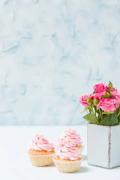 Bouquet of pink roses in retro shabby chic vase and cupcake with cream decoration. — Stock Photo, Image