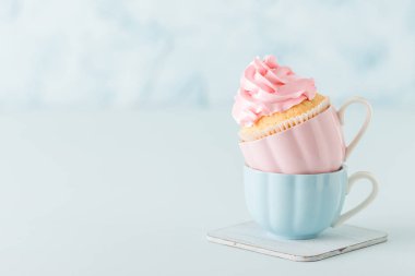 Kek krem dekorasyonda pembe pastel mavi zemin üzerine iki bardak ile.