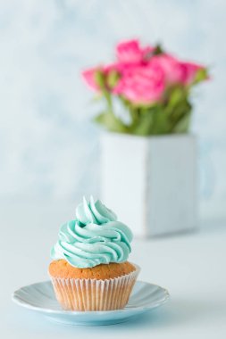 Mavi pastel dikey afiş ile dekore edilmiş cupcake ve retro eski püskü şık vazoda pembe gül buketi.