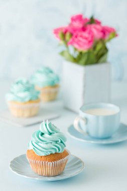 Mavi pastel dikey afiş ile dekore edilmiş cupcakes, sütlü kahve fincan ve pembe gül buketi.