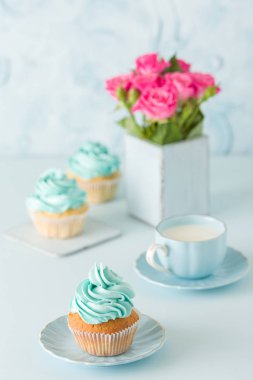 Mavi pastel dikey afiş ile dekore edilmiş cupcakes, sütlü kahve fincan ve pembe gül buketi.