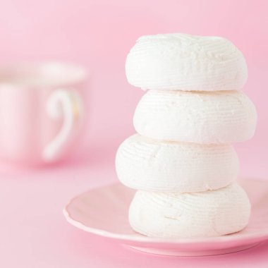 Zephyr'i dessrt pembe plaka, pastel pembe arka plan üzerine sütlü kahve fincan beyaz. Güzel tatlılar. Kare afiş, tebrik kartı için doğum günü, düğün. Fotoğraf kadar kapatın. Seçici odak