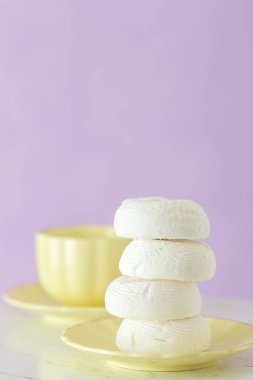 Zephyr'i dessrt sarı plaka, pastel mor zemin üzerine sütlü kahve fincan beyaz. Güzel tatlılar. Dikey afiş, tebrik kartı için doğum günü, düğün. Fotoğraf kadar kapatın. Seçici odak