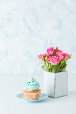 Mavi pastel dikey afiş ile cupcake mavi dekorasyon ve retro eski püskü şık vazoda pembe gül buketi.