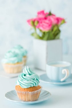 Mavi pastel dikey afiş ile dekore edilmiş cupcakes, sütlü kahve fincan ve pembe gül buketi.