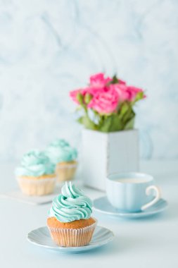 Mavi pastel dikey afiş ile dekore edilmiş cupcakes, sütlü kahve fincan ve pembe gül buketi.