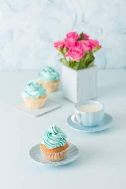 Mavi pastel dikey afiş ile dekore edilmiş cupcakes, sütlü kahve fincan ve pembe gül buketi.