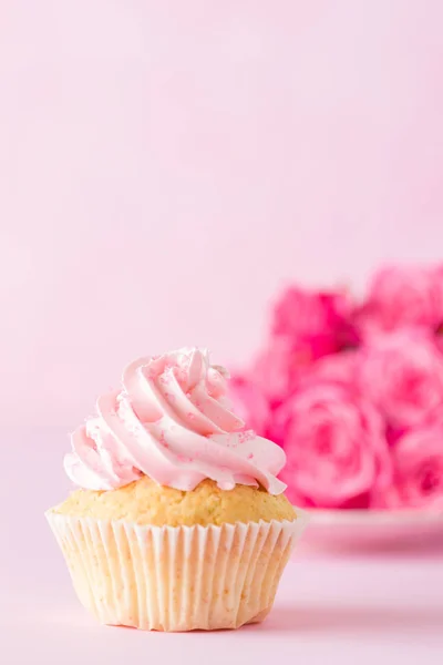 Cupcake con decoración de crema rosa y rosas sobre fondo pastel rosa . — Foto de Stock