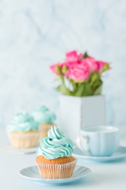 Mavi pastel dikey afiş ile dekore edilmiş cupcakes, sütlü kahve fincan ve pembe gül buketi.