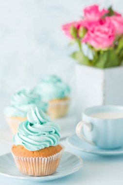 Mavi pastel dikey afiş ile dekore edilmiş cupcakes, sütlü kahve fincan ve pembe gül buketi.