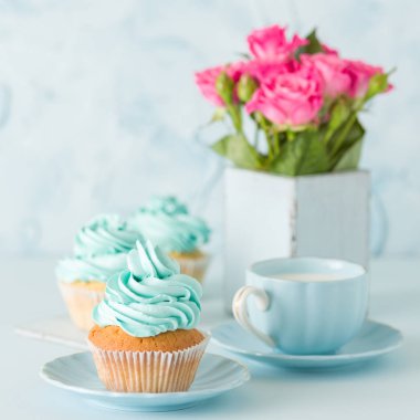 Mavi pastel afiş ile dekore edilmiş cupcakes, sütlü kahve fincan ve pembe gül buketi.