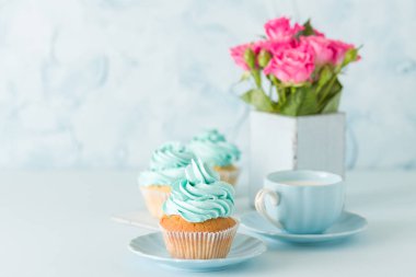 Mavi pastel afiş ile dekore edilmiş cupcakes, sütlü kahve fincan ve pembe gül buketi.