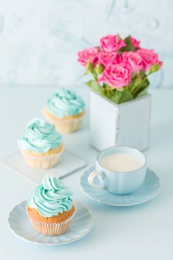 Mavi pastel dikey afiş ile dekore edilmiş cupcakes, sütlü kahve fincan ve pembe gül buketi.