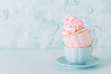 Pastel mavi zemin üzerine iki su bardağı hafif pembe krem süslemeli cupcake.