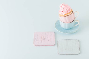 Pastel mavi zemin üzerine iki su bardağı hafif pembe krem süslemeli cupcake.