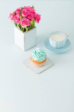 Cupcake pastel mavi zemin üzerine retro eski püskü şık vazoda nazik mavi krem ve pembe Gül ile.