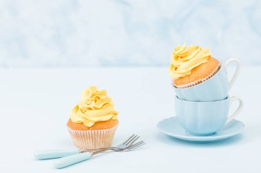 Pastel mavi zemin üzerine iki küçük bardak tatlı sarı krem süslemeli cupcake.