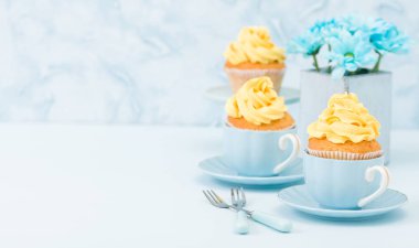 Cupcake ihale sarı krem dekorasyon ve retro eski püskü şık vazoda pastel mavi zemin üzerine mavi papatya buketi ile.