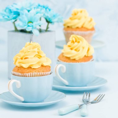 Cupcake ihale sarı krem dekorasyon ve retro eski püskü şık vazoda pastel mavi zemin üzerine mavi papatya buketi ile.