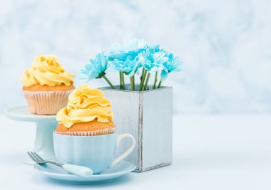 Cupcake ihale sarı krem dekorasyon ve retro eski püskü şık vazoda pastel mavi zemin üzerine mavi papatya buketi ile.