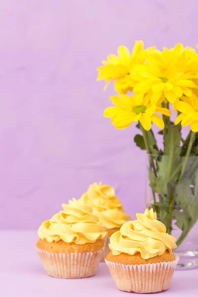 Żółta Chryzantema w szkło i ciastko z żółty krem na fioletowym tle pastel. Kwiaty i deser dzień matki układ projektowania. — Zdjęcie stockowe