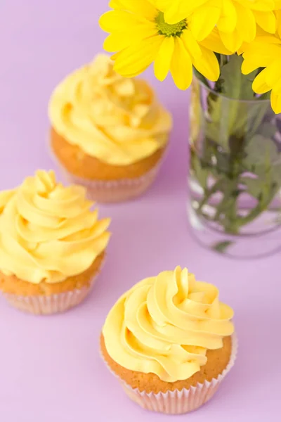 Желтый хризантем в стекле и кекс с желтым кремом на фиолетовом пастельном фоне. Дизайн Дня матери с цветами и десертом . — стоковое фото