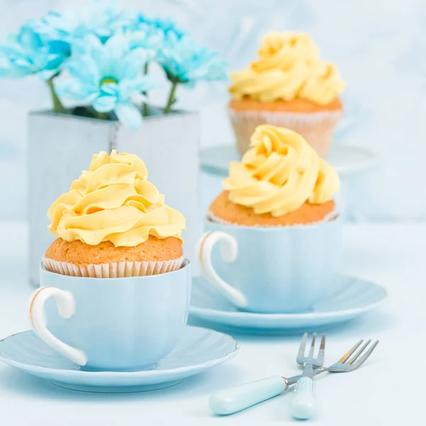 Cupcake with tender yellow cream decoration and bouquet of blue chrysanthemum in retro shabby chic vase on blue pastel background. — Stock Photo, Image