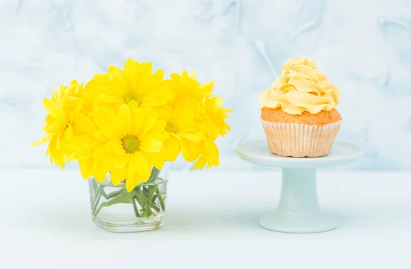 Cupcake com doce decoração creme amarelo e buquê de crisântemo amarelo em vaso chique retro gasto em fundo pastel azul . — Fotografia de Stock