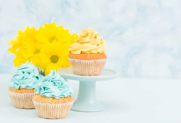 Cupcake com doce decoração creme amarelo e buquê de crisântemo amarelo em vaso chique retro gasto em fundo pastel azul . — Fotografia de Stock