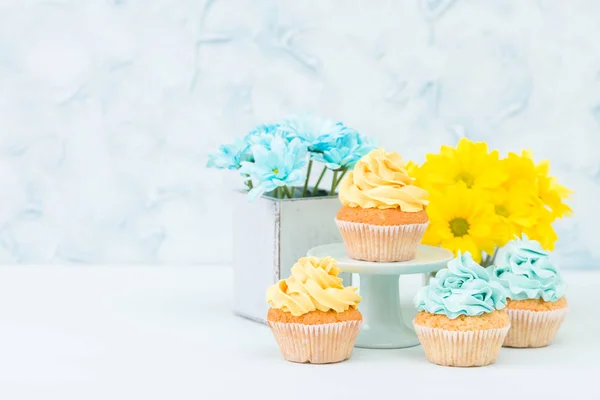 Cupcake with yellow and blue cream decoration and bouquet of yellow and blue chrysanthemum. Stilllife and minimalism concept