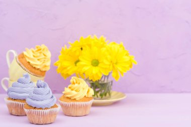 Sarı ve mor krem ve Kasımpatı Menekşe pastel arka planda tebrik kartı copyscape ile süslenmiş cupcakes.