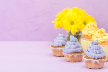 Sarı ve mor krem ve Kasımpatı Menekşe pastel arka planda tebrik kartı copyscape ile süslenmiş cupcakes.