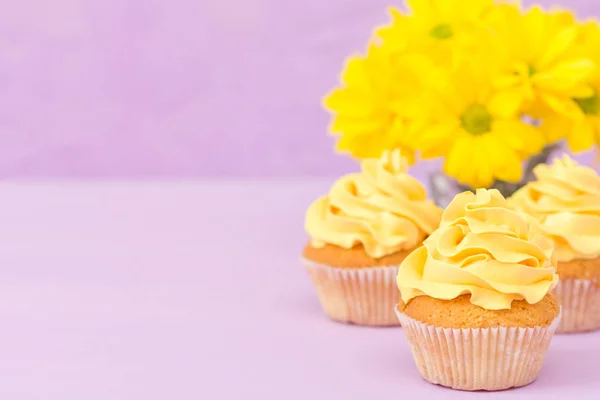 Cupcakes decorados con crema amarilla y crisantemos sobre fondo pastel violeta para tarjeta de felicitación con copyscape . — Foto de Stock