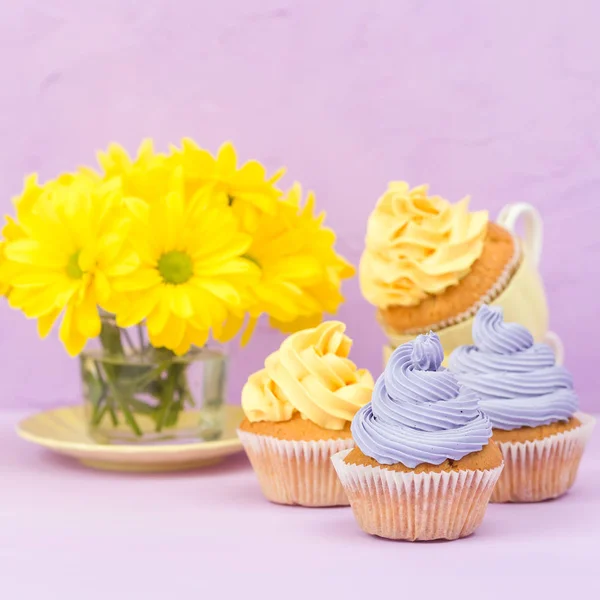 Cupcakes decorados com creme amarelo e violeta e crisântemos em fundo pastel violeta para cartão de saudação com copyscape . — Fotografia de Stock