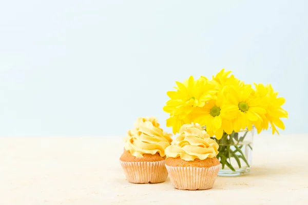 Cupcake with sweet yellow cream decoration and bouquet of yellow chrysanthemum in small glass