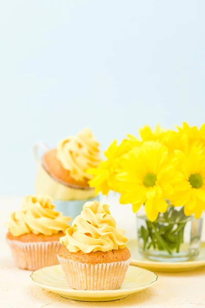 Cupcake with yellow cream decoration and bouquet of yellow chrysanthemum in small glass.