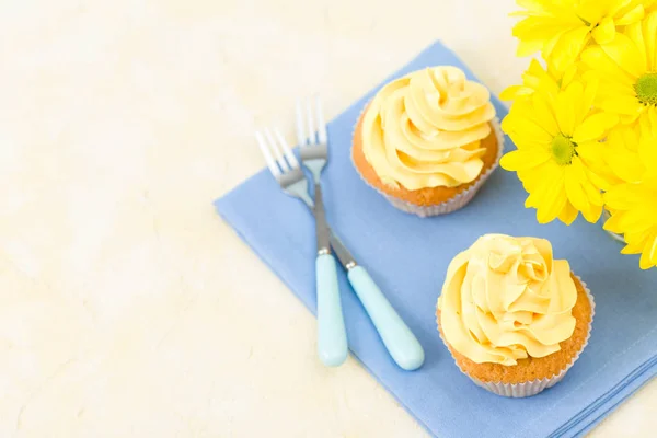 Cupcake with yellow cream decoration on blue napkin and bouquet of yellow chrysanthemum in small glass. — Stock Photo, Image