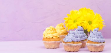 Sarı ve mor krem ve Kasımpatı tebrik afiş için metin alanı Menekşe pastel zemin üzerine buket cupcakes süslenmiş.