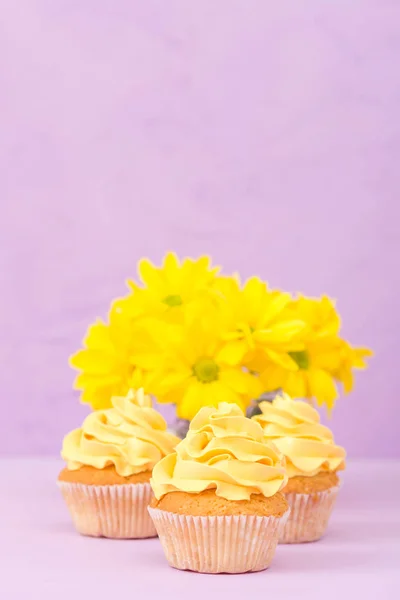 Cupcakes decorados com creme amarelo e crisântemos em fundo pastel violeta para cartão de saudação com copyscape . — Fotografia de Stock