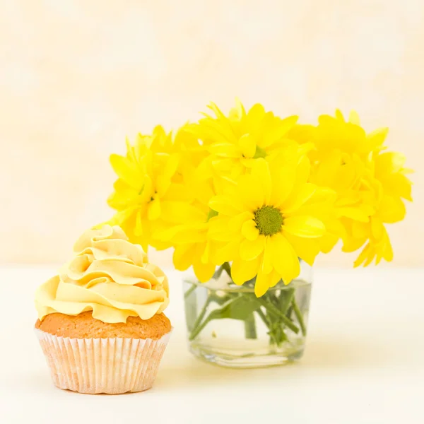 Кекс с нежным желтым кремом украшения и букет хризантемы в стекле на желтом пастельном фоне . — стоковое фото