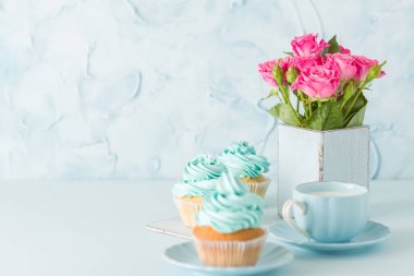 Mavi pastel yatay afiş ile dekore edilmiş cupcakes, sütlü kahve fincan ve pembe gül buketi.