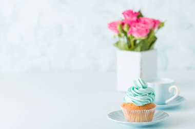 Mavi pastel afiş ile dekore edilmiş cupcakes, sütlü kahve fincan ve pembe gül buketi.