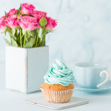 Cupcake pastel mavi zemin üzerine retro eski püskü şık vazoda nazik mavi krem ve pembe Gül ile.