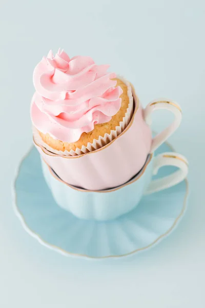 Cupcake con suave decoración de crema rosa en dos tazas sobre fondo de pastel azul . — Foto de Stock
