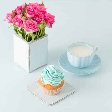 Cupcake pastel mavi zemin üzerine retro eski püskü şık vazoda nazik mavi krem ve pembe Gül ile.