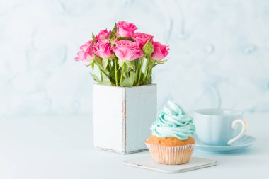 Cupcake pastel mavi zemin üzerine retro eski püskü şık vazoda nazik mavi krem ve pembe Gül ile.